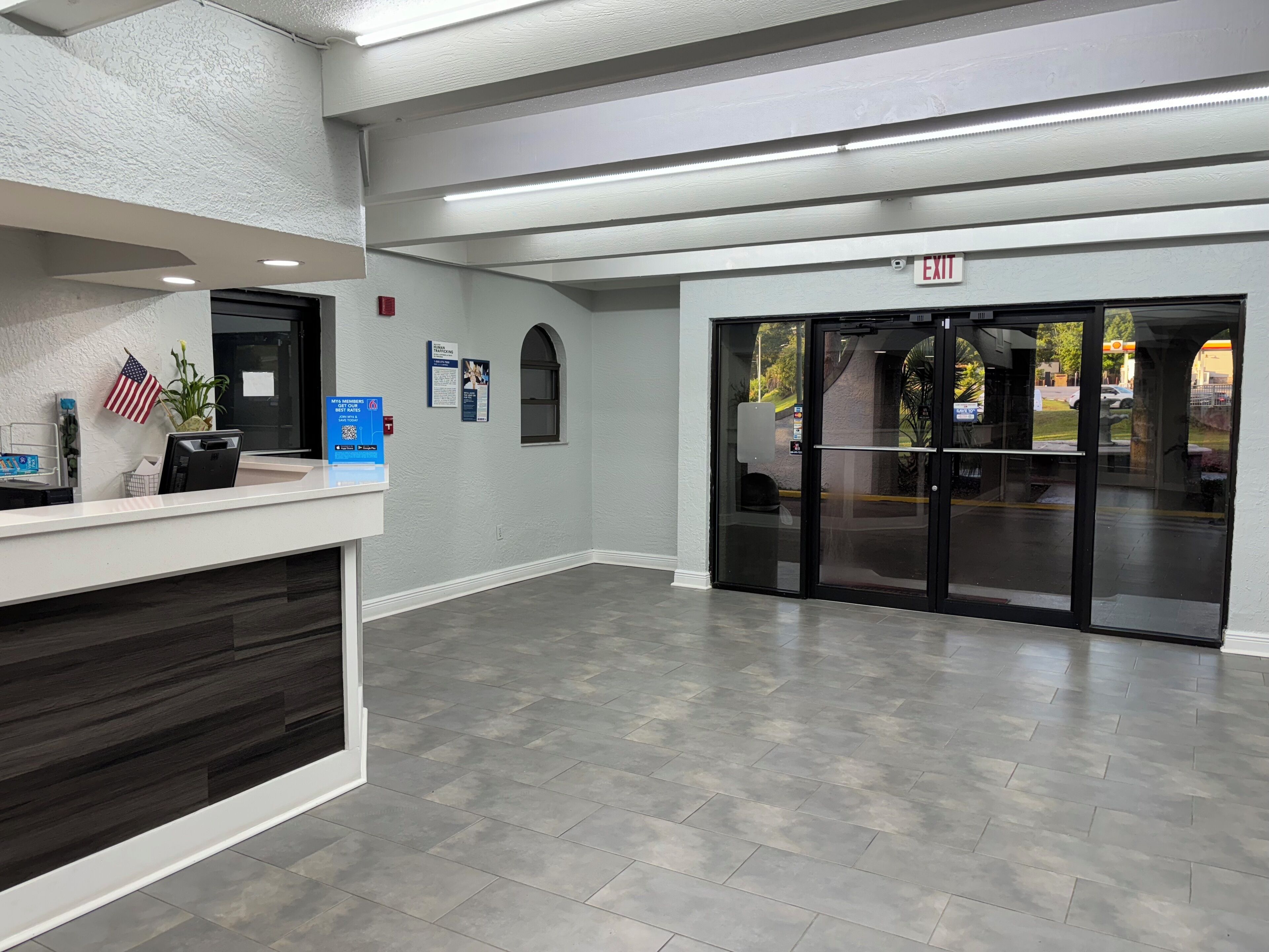 A reception area with a counter, an American flag, a plant, and an exit sign.