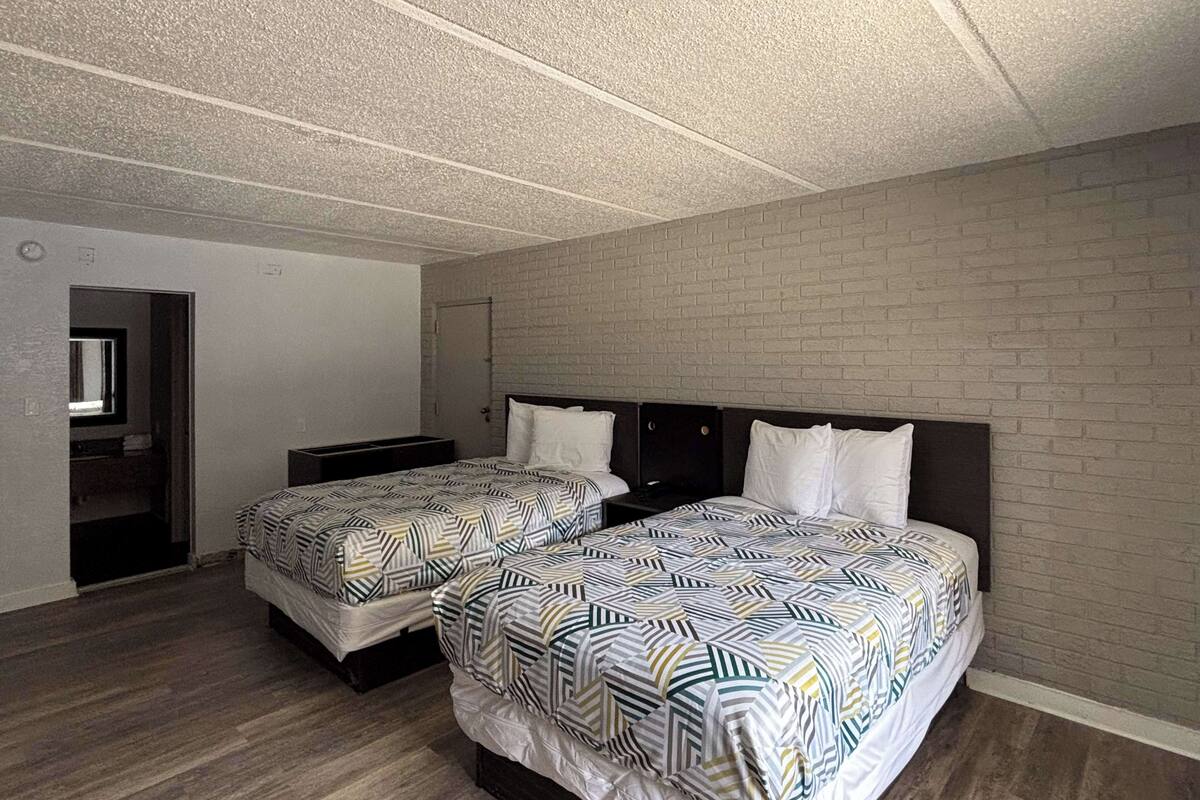 A room with two beds, a brick wall, and a wooden floor.