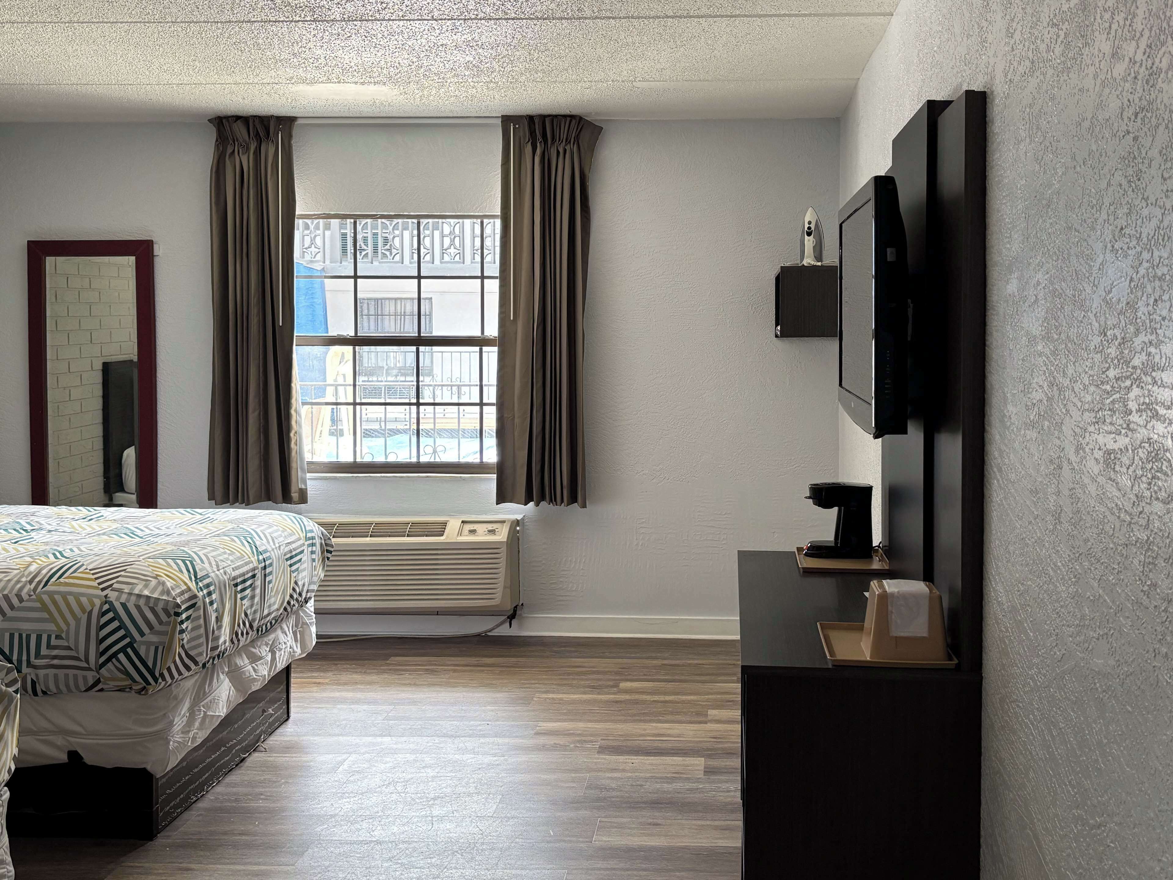 Quarto de hotel com cama, janela com cortinas, televisão presa à parede e aquecedor.