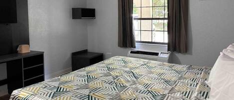 A bedroom with a bed, a TV mounted on the wall, a window with curtains, and a heater.