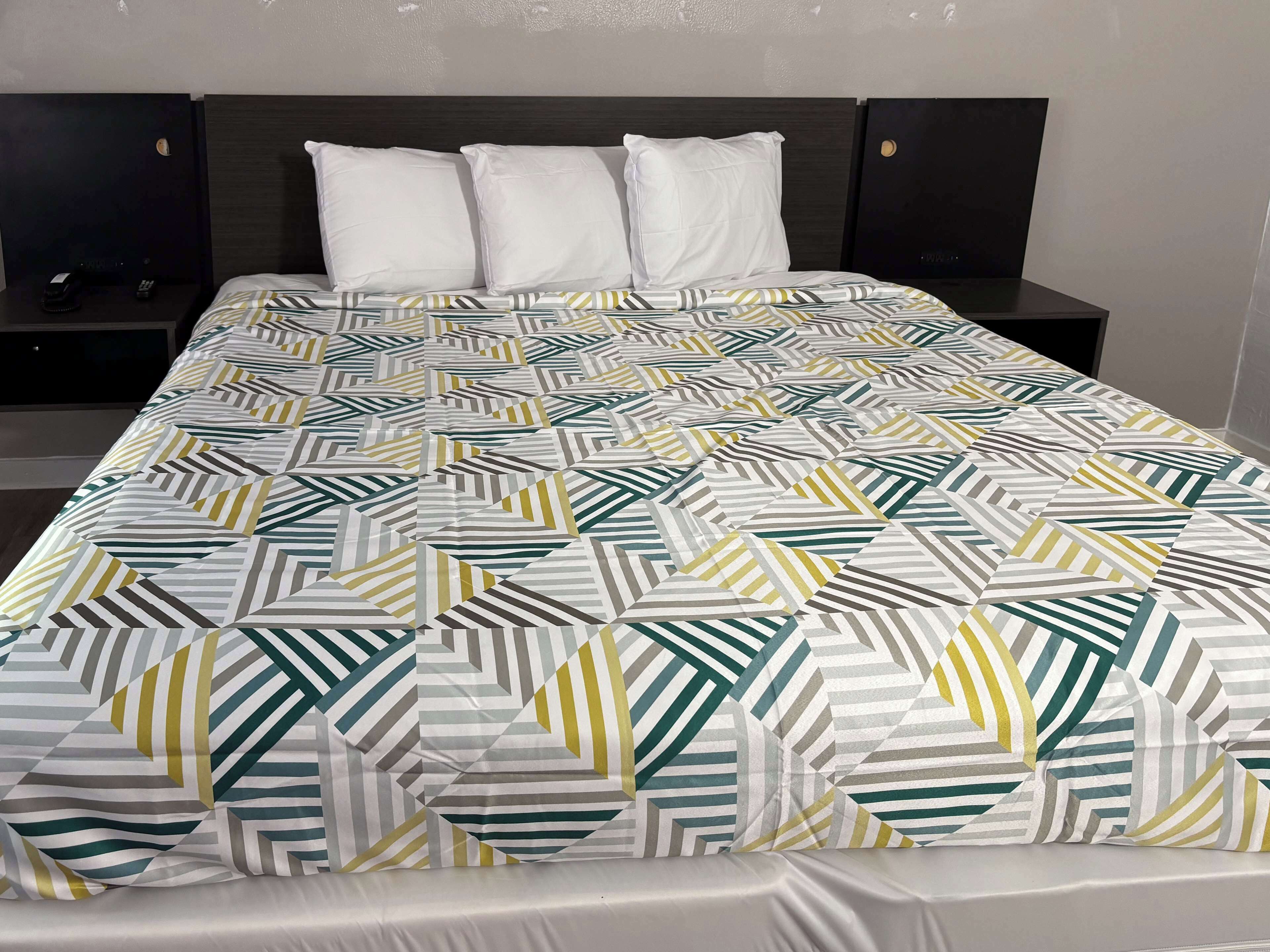 Een netjes opgemaakt bed met een bedsprei met dessin, twee nachtkastjes met donkerhouten afwerking, en een effen muur op de achtergrond.