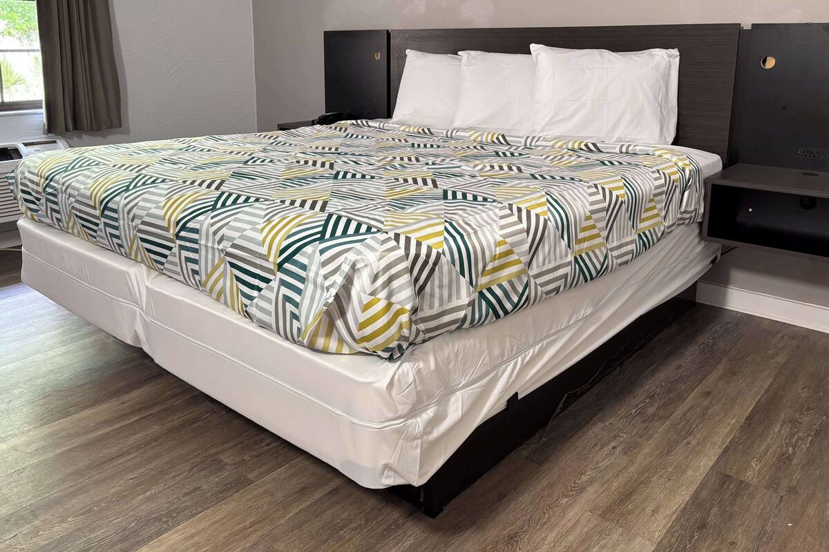 A neatly made bed with a patterned bedspread, a white pillow, and a dark headboard.