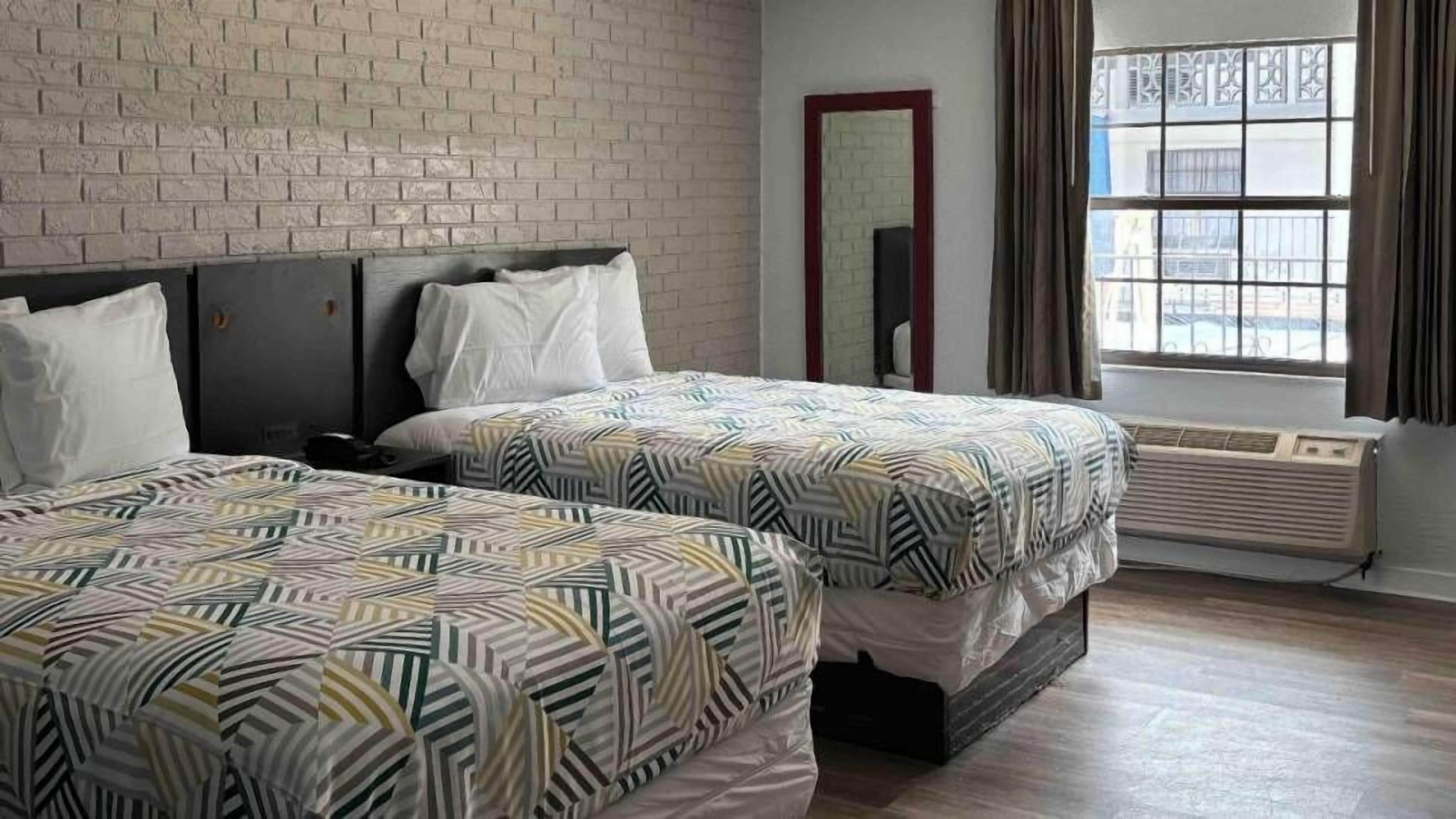 Una habitación de hotel con dos camas, una pared de ladrillo, un ventanal con cortinas y un espejo.