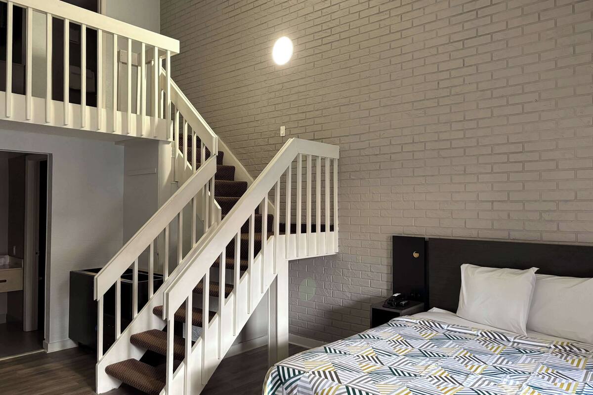 A modern bedroom with a loft-style staircase, a bed with patterned bedding, and a brick wall.