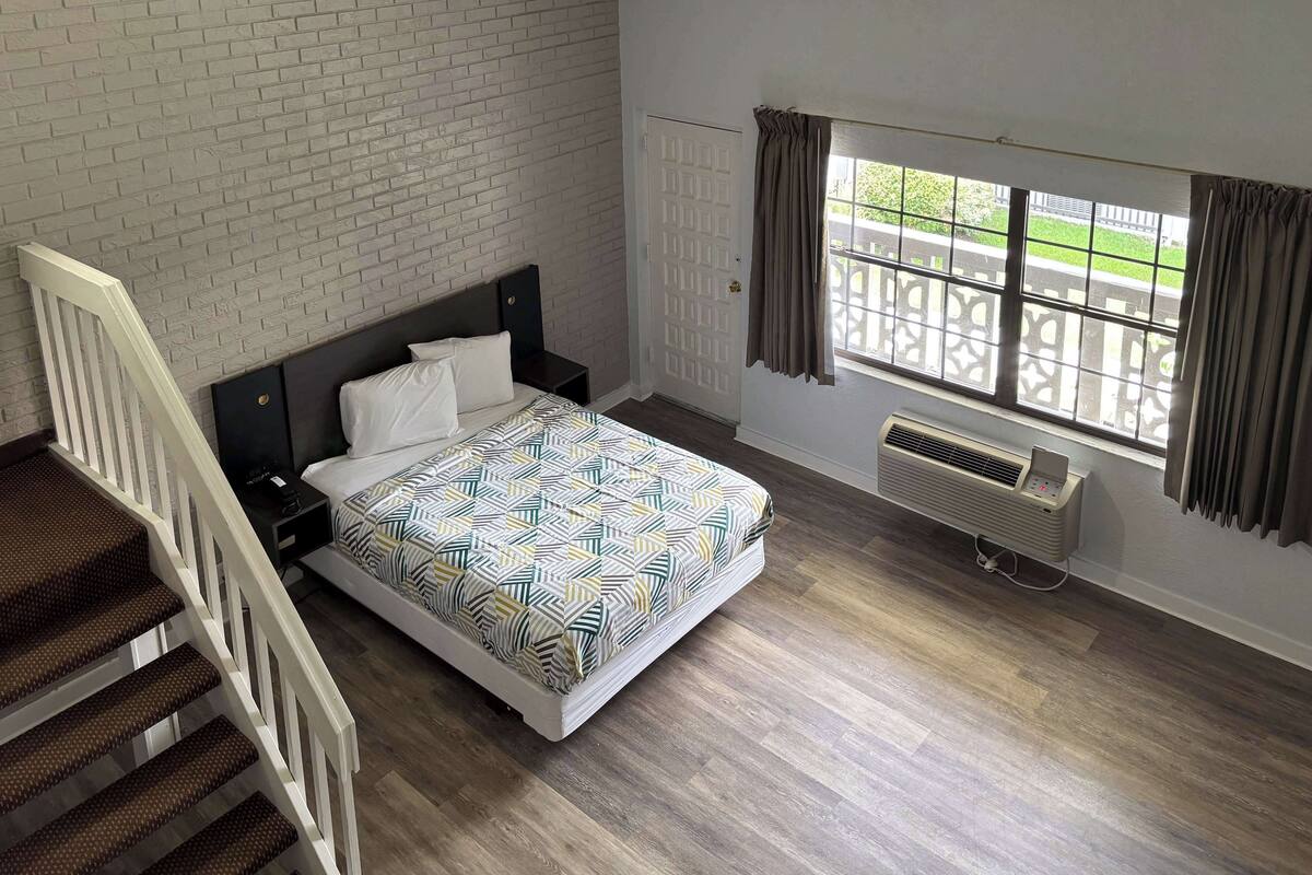 A bedroom with a bed, a window with curtains, a radiator, and a staircase.