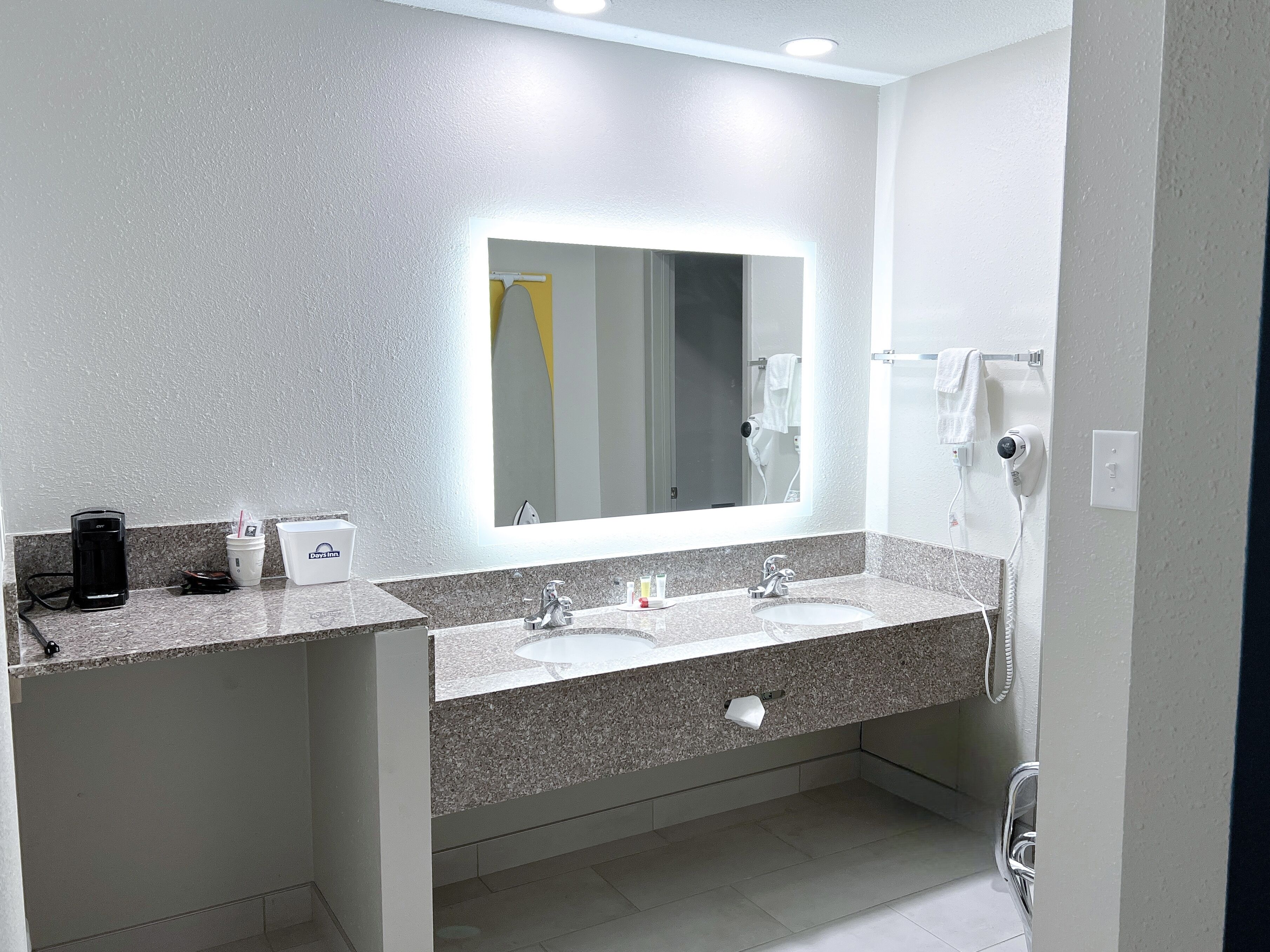 Une salle de bain moderne équipée de deux lavabos, d’un grand miroir, d’un sèche-cheveux et d’une machine à café.