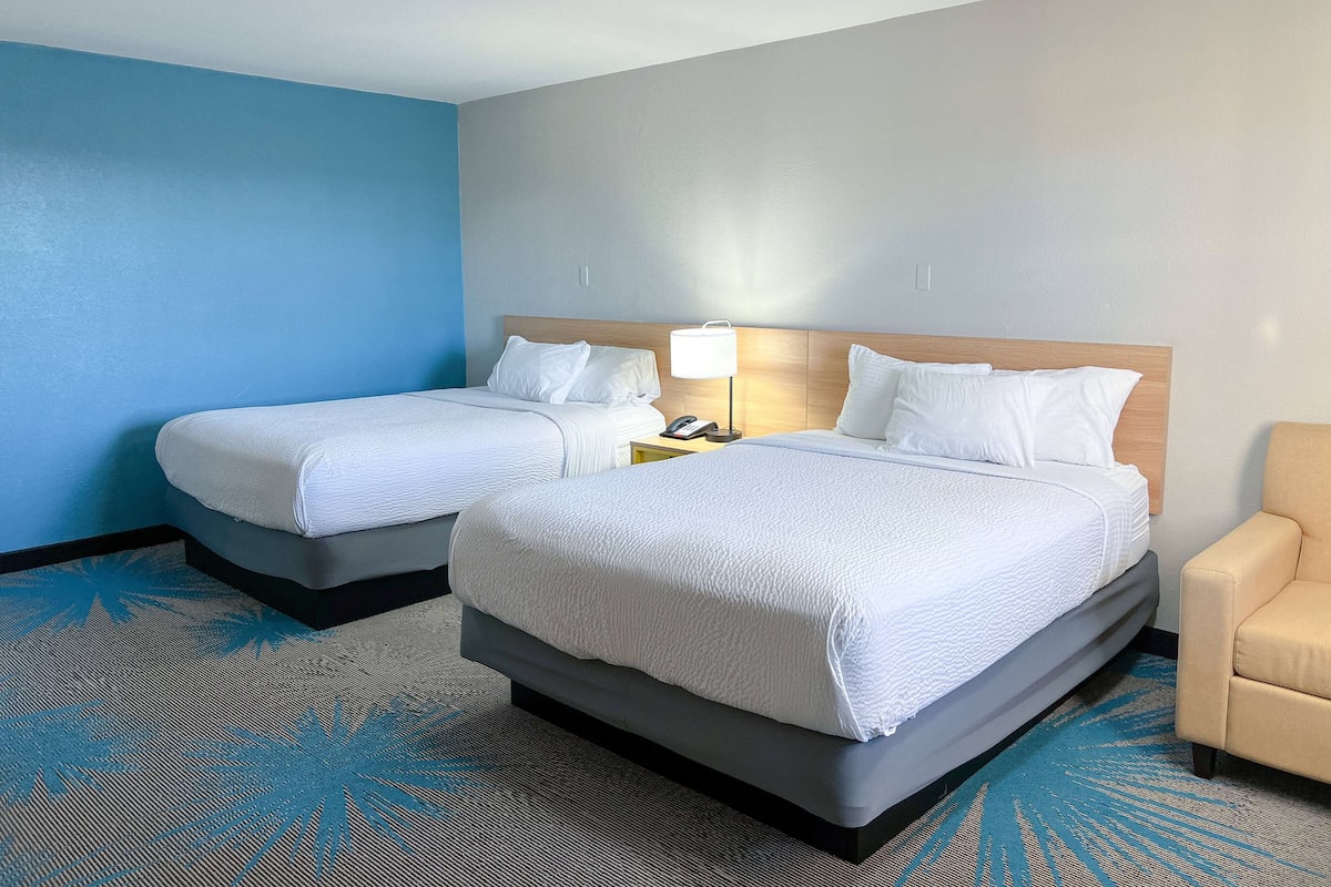 A hotel room with two beds, a nightstand, a lamp, and a chair.