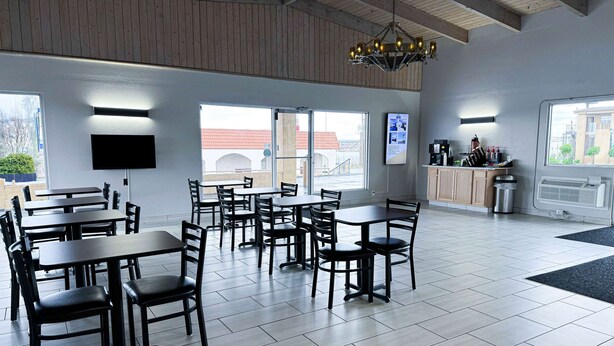 A spacious dining area with multiple tables and chairs, a chandelier, a television mounted on the wall, and large windows offering a view of the outside. - Days Inn & Suites by Wyndham Santa Rosa (Santa Rosa)