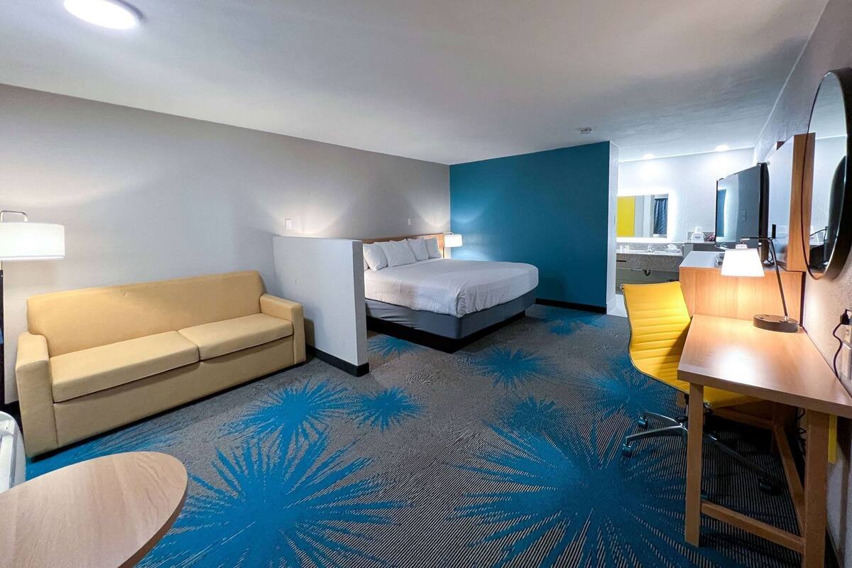 A hotel room with a bed, a sofa, a desk, and a bathroom visible through an open door.