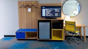 A hotel room with a wooden wardrobe, a TV mounted on it, a small fridge, a desk with a chair, a mirror, and a carpet with a blue pattern. - Days Inn & Suites by Wyndham Santa Rosa (Santa Rosa)