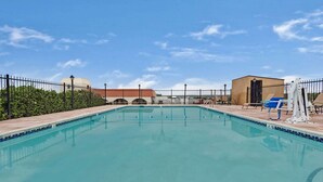 A swimming pool with a tiled edge, surrounded by a fence, and a building with a dome roof in the background. - Days Inn & Suites by Wyndham Santa Rosa (Santa Rosa)