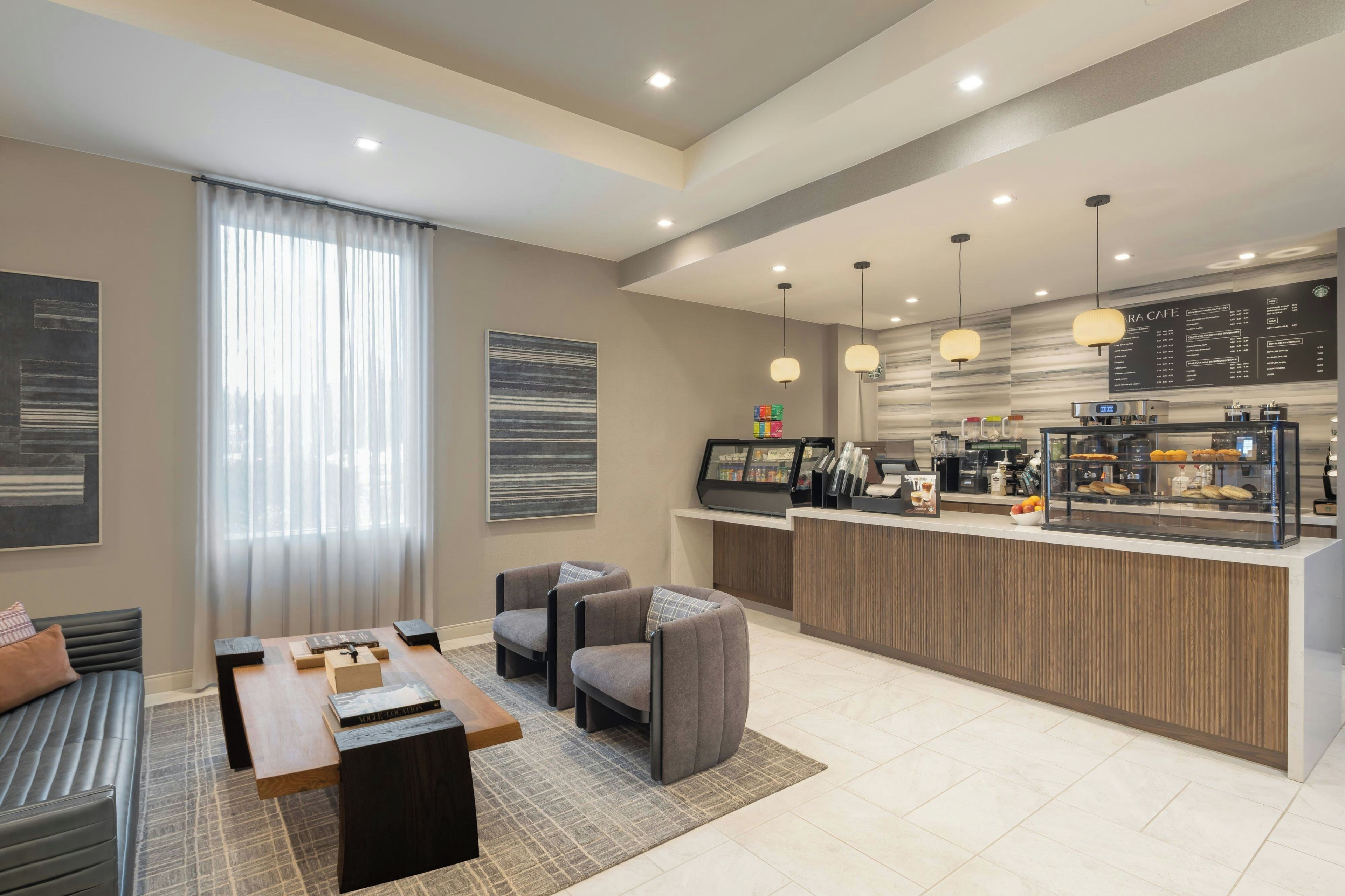 A modern hotel lobby with a seating area, a coffee bar, and a large window with curtains.