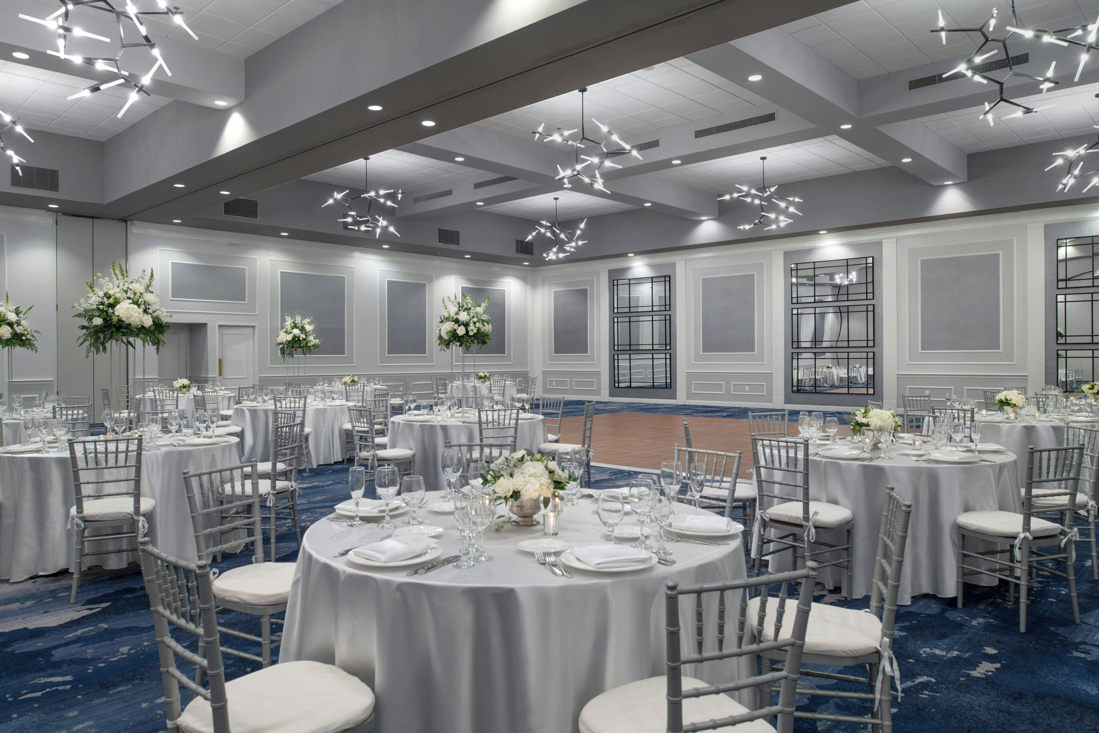 A banquet hall with round tables, white chairs, and floral centerpieces.
