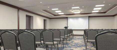 A conference room with rows of chairs, a projector screen, and a carpeted floor.