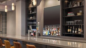 A bar area with a long counter, multiple stools, shelves with bottles and glasses, and a large screen. - Renaissance Framingham Hotel & Conference Center (Framingham)