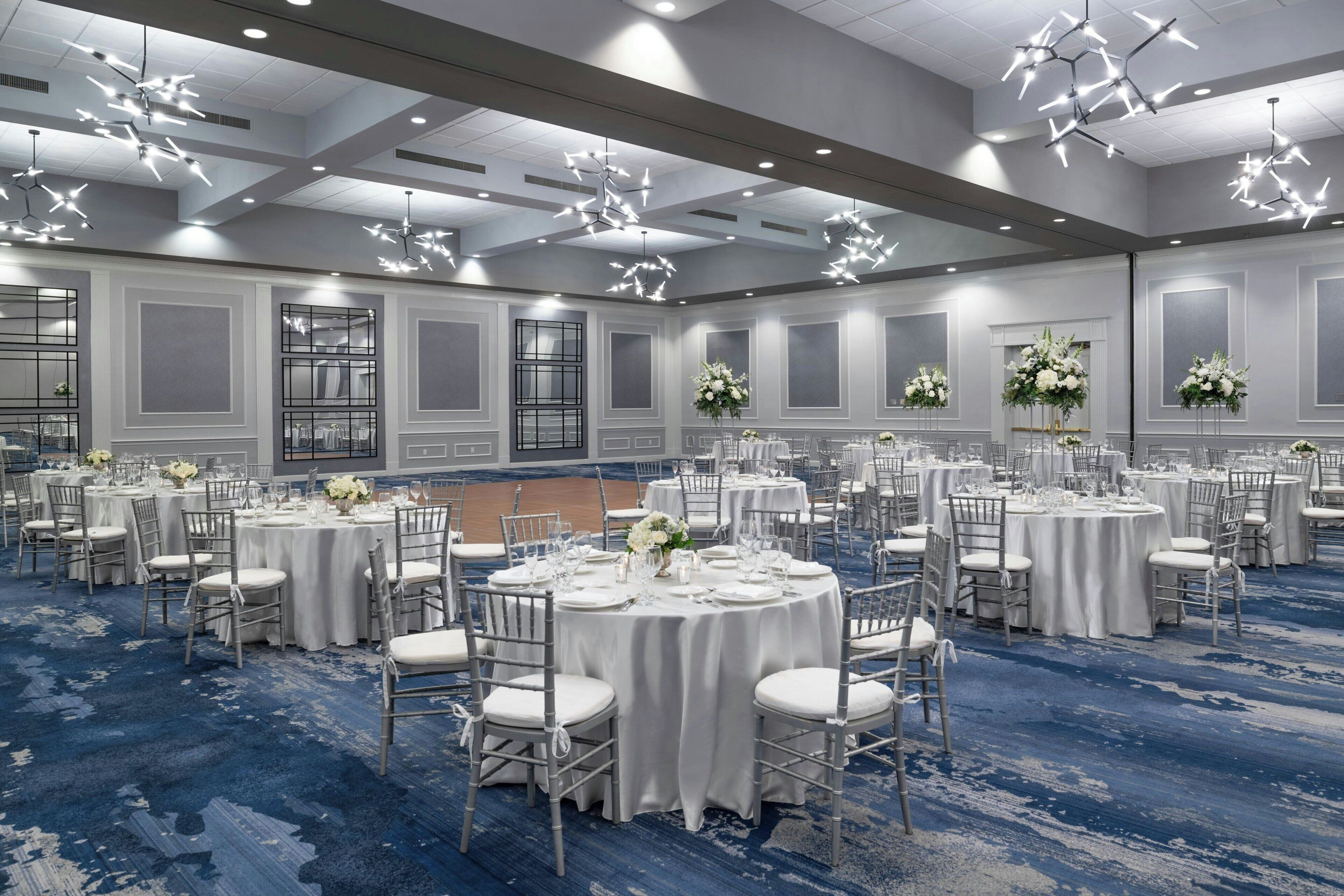 A large banquet hall with round tables set for dining, white chairs, and floral centerpieces.