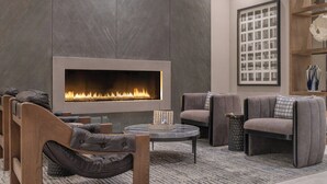 A modern living room with a large fireplace, comfortable seating, and a decorative wall piece. - Renaissance Framingham Hotel & Conference Center (Framingham)