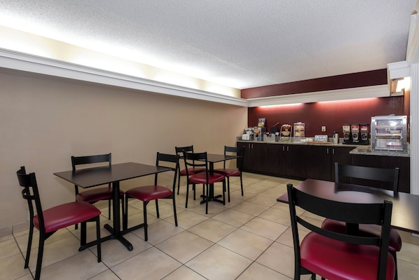 Un restaurante con mesas y sillas, una barra con alimentos y una máquina de café.