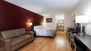 A hotel room with a bed, a sofa, a desk with a lamp, a TV, and a picture on the wall.