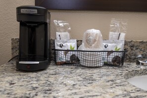 Een koffiezetapparaat en een mand met wegwerpbekers op een granieten aanrecht.