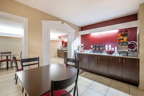 Un comedor con mesa y sillas, una cocina con cafetera, y una encimera con varios objetos.