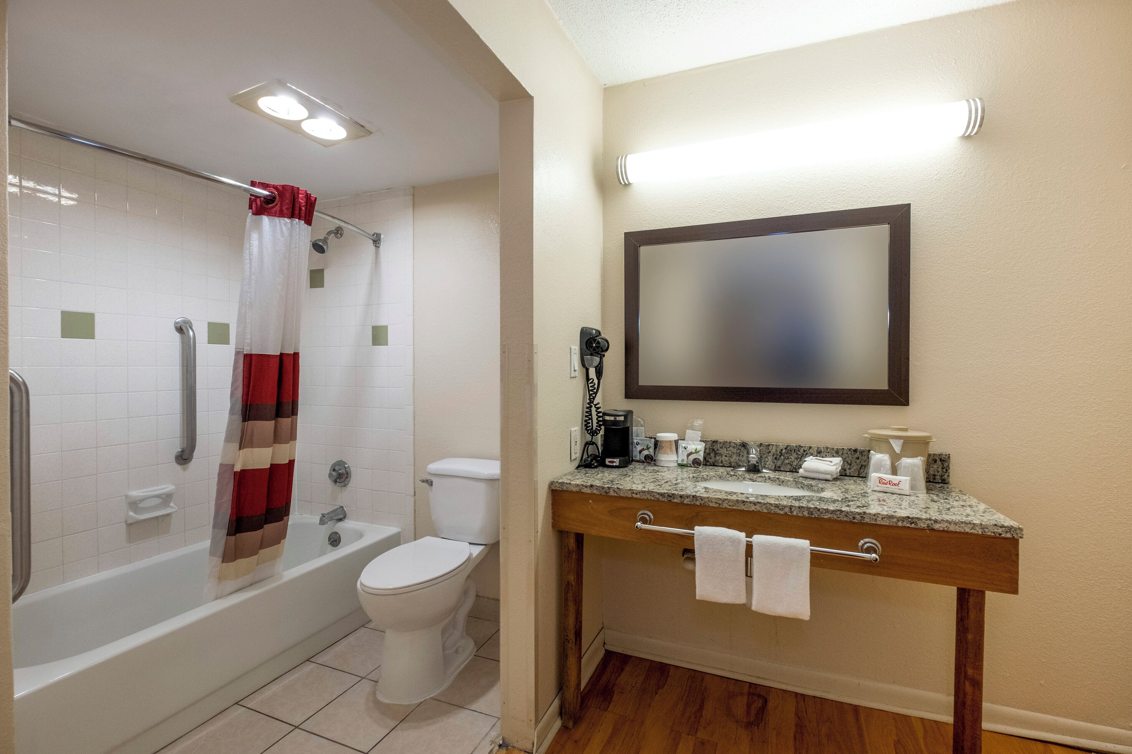 Un baño con bañera, inodoro y zona de ducha. Cuenta con un tocador, un espejo y un perchero.