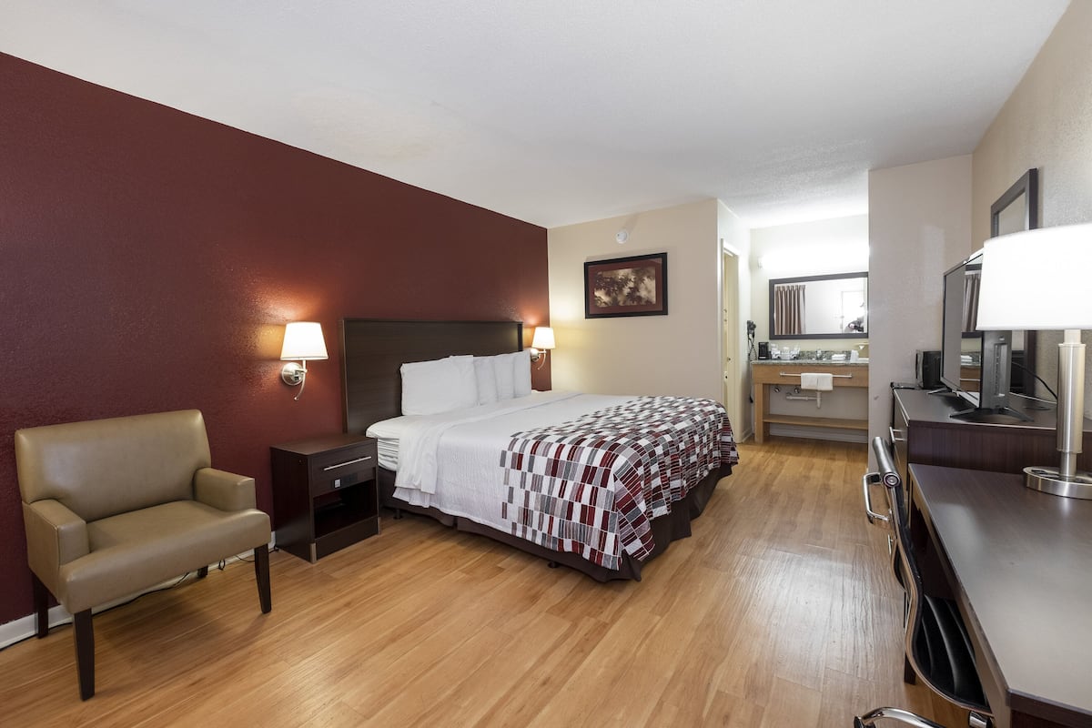 A hotel room with a bed, a chair, a desk, a mirror, and a television.