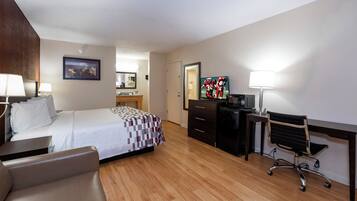 A hotel room with a bed, a desk, a chair, a television, and a desk lamp.