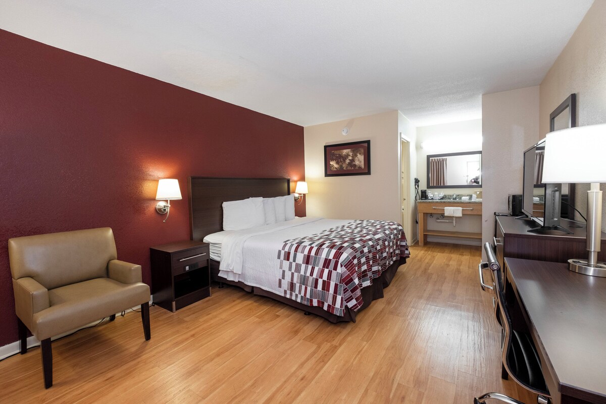 A hotel room with a bed, a chair, a desk, a mirror, and a bathroom.