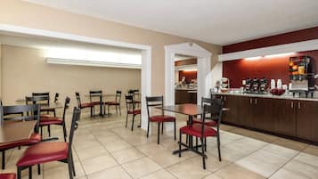 Un comedor de hotel con mesas y sillas, una zona de cocina con cafeteras y un mostrador con dispensador de bebidas.