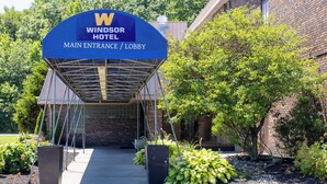 Hoofdingang van Hotel Windsor met overdekte doorgang, een bakstenen gebouw en omliggend groen.