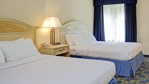 Een hotelkamer met twee bedden, een nachtkastje met een lamp en een raam met gordijnen.