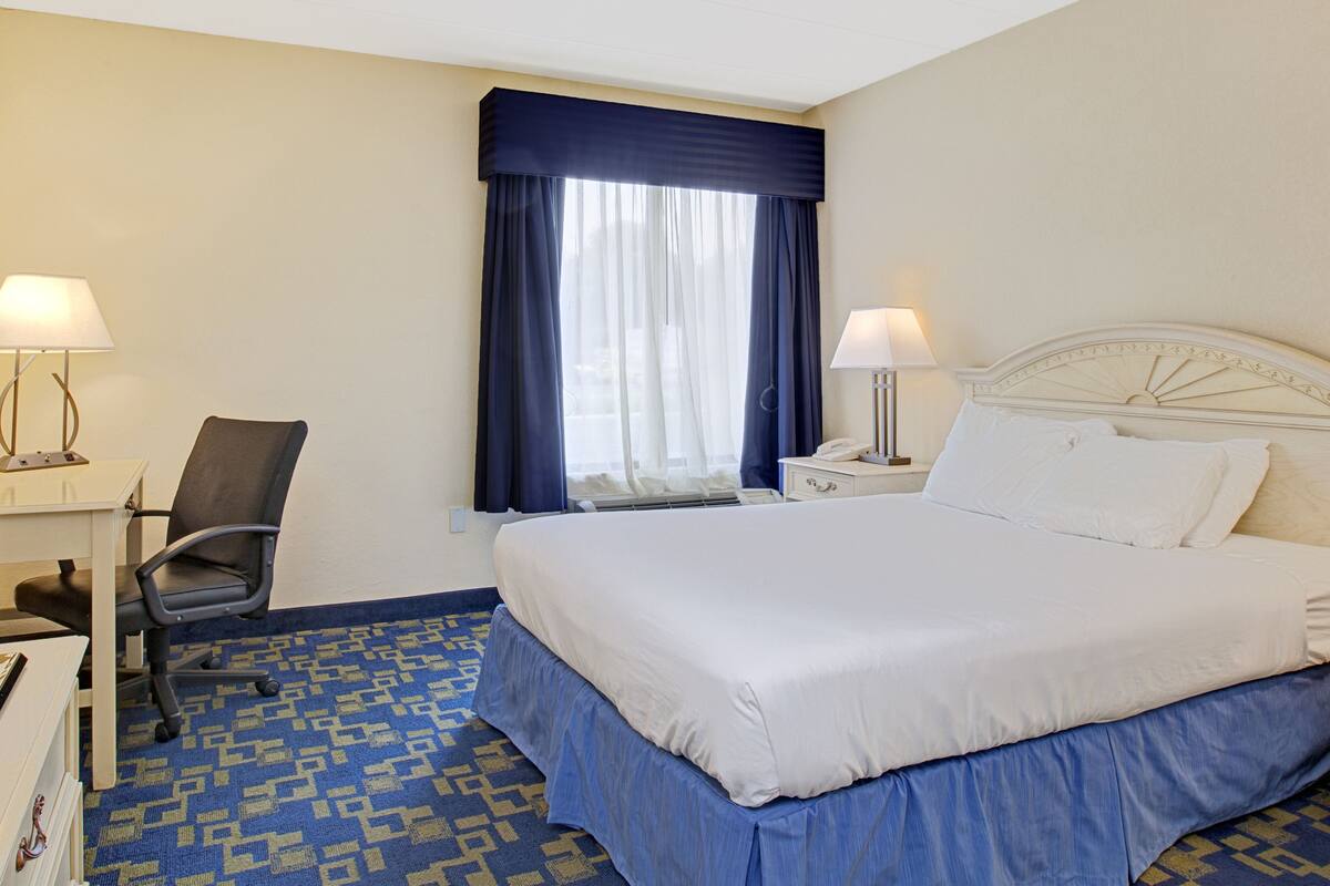 A hotel room with a large bed, a desk with a chair, a nightstand, and two lamps.