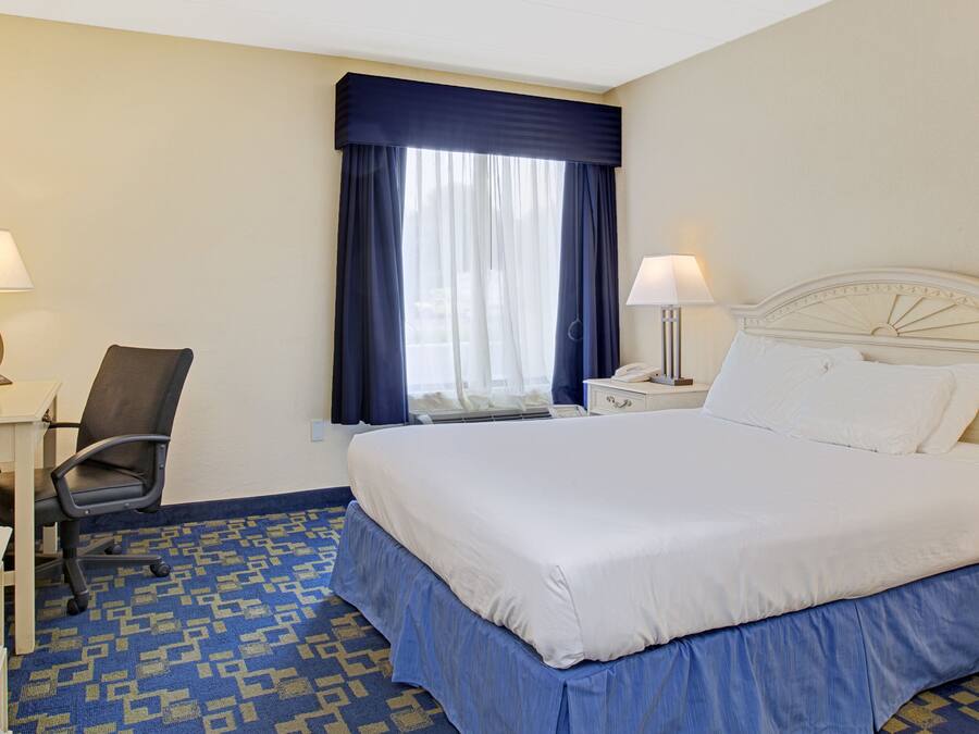 A hotel room with a large bed, a desk with a chair, a nightstand, and two lamps.