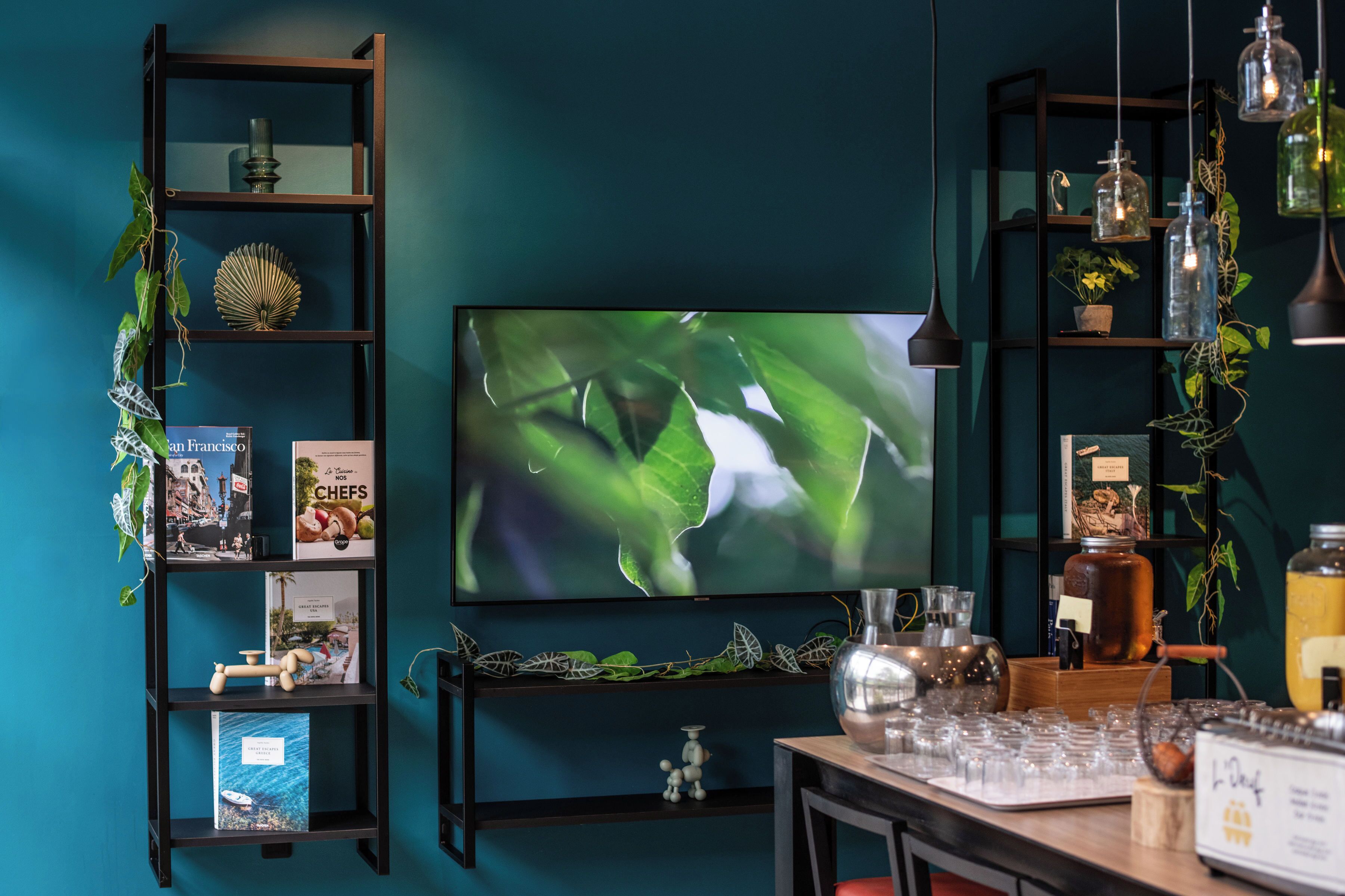 A modern living room with a teal wall, a flat-screen TV, dark wooden shelves, and a coffee table with glassware.