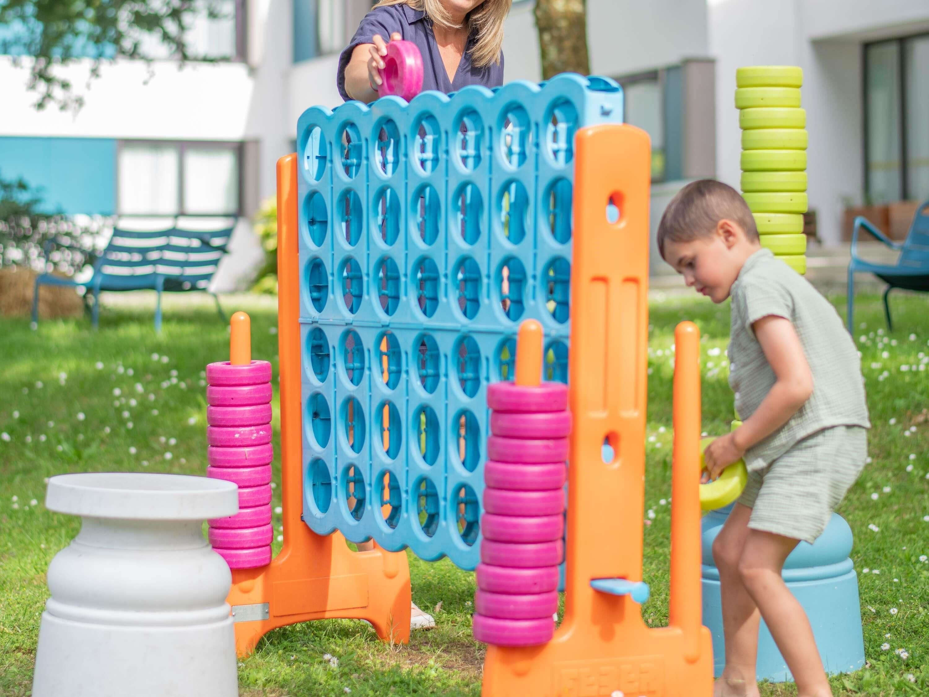 Un enfant joue avec un jeu d’extérieur coloré dans un espace herbeux, avec un bâtiment en arrière-plan.