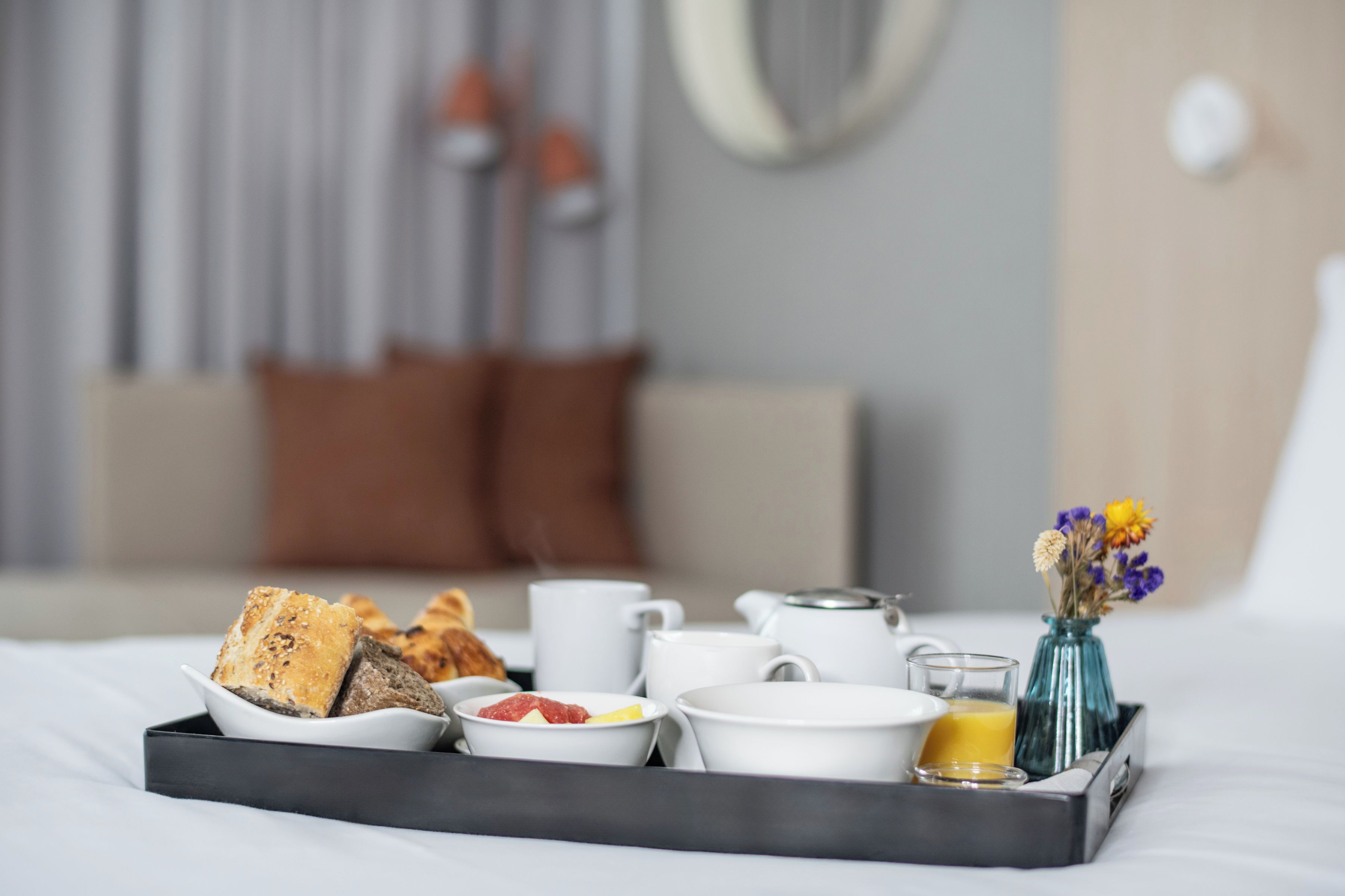 A breakfast tray with bread, fruit, and beverages on a bed in a hotel room.