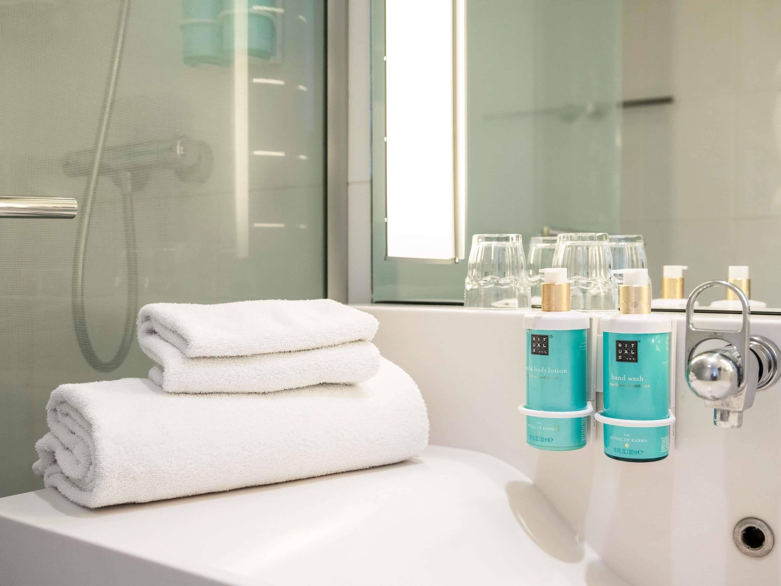 A bathroom with a bathtub, two rolled towels, and two bottles of hand wash soap.