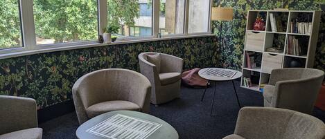 A room with a large window, two armchairs, a small table, a bookshelf, and a patterned rug.