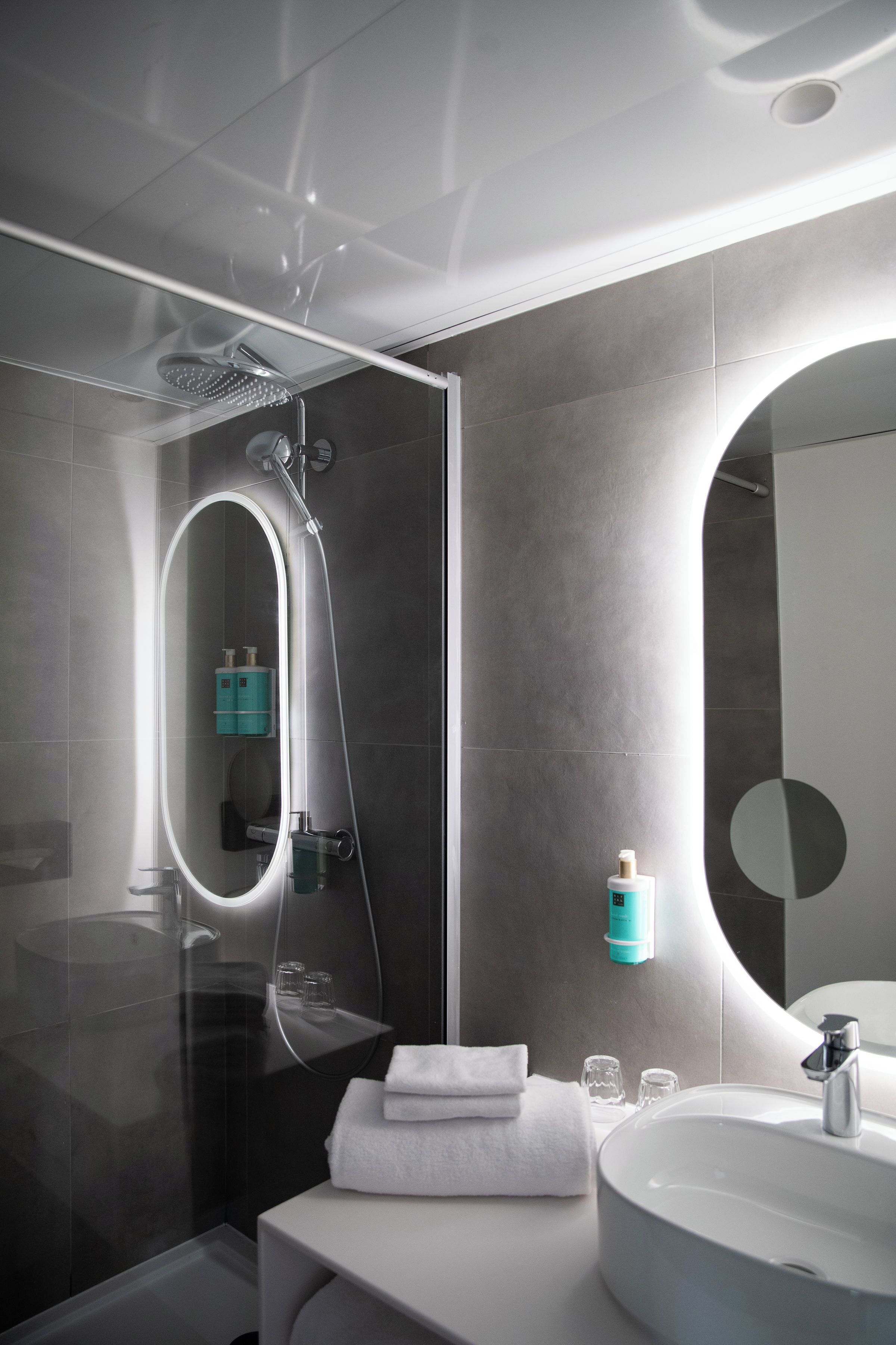 Een moderne badkamer met een douche met glazen wand, een witte wastafel en een grote spiegel.