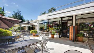 Un patio al aire libre con mesas, sillas, plantas en macetas y un escaparate de vidrio.