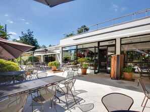 An outdoor patio area with tables and chairs, potted plants, and a glass storefront.
