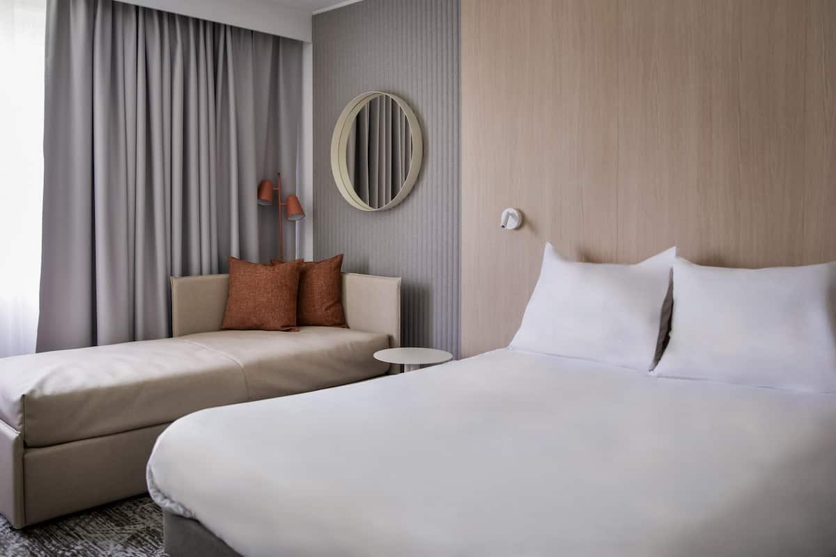 A hotel room with two beds, a small table, a lamp, and a mirror on the wall.