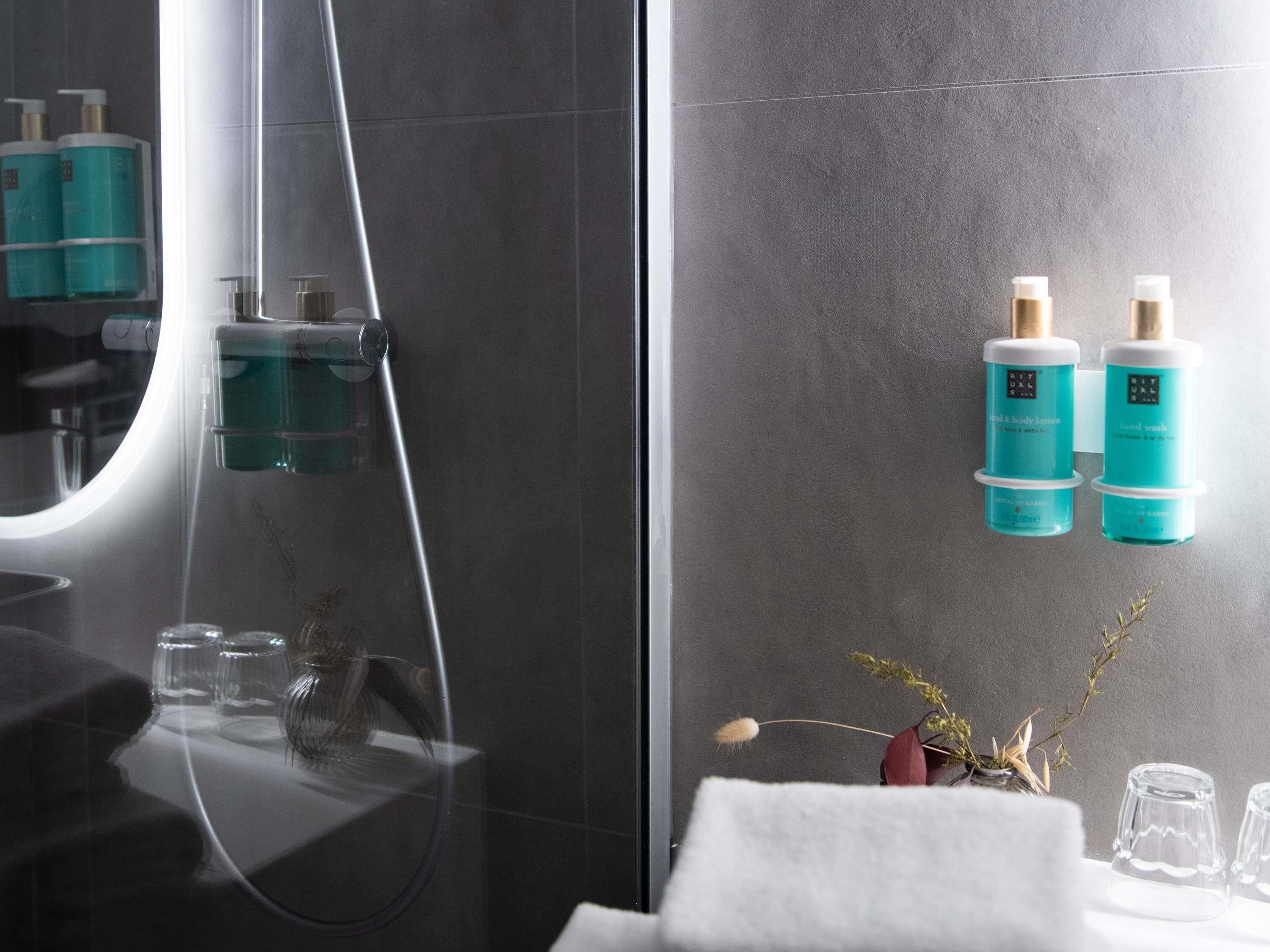 Un baño moderno con cabina de ducha de vidrio, un espejo y dos botellas de jabón de manos en la pared.