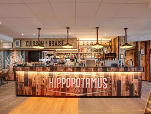 Una zona de bar con mostrador de madera, señalización con la marca y luces colgantes.