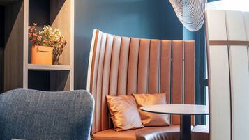 A modern interior with a wooden shelving unit, a cushioned bench, a round table, and a unique hanging light fixture.
