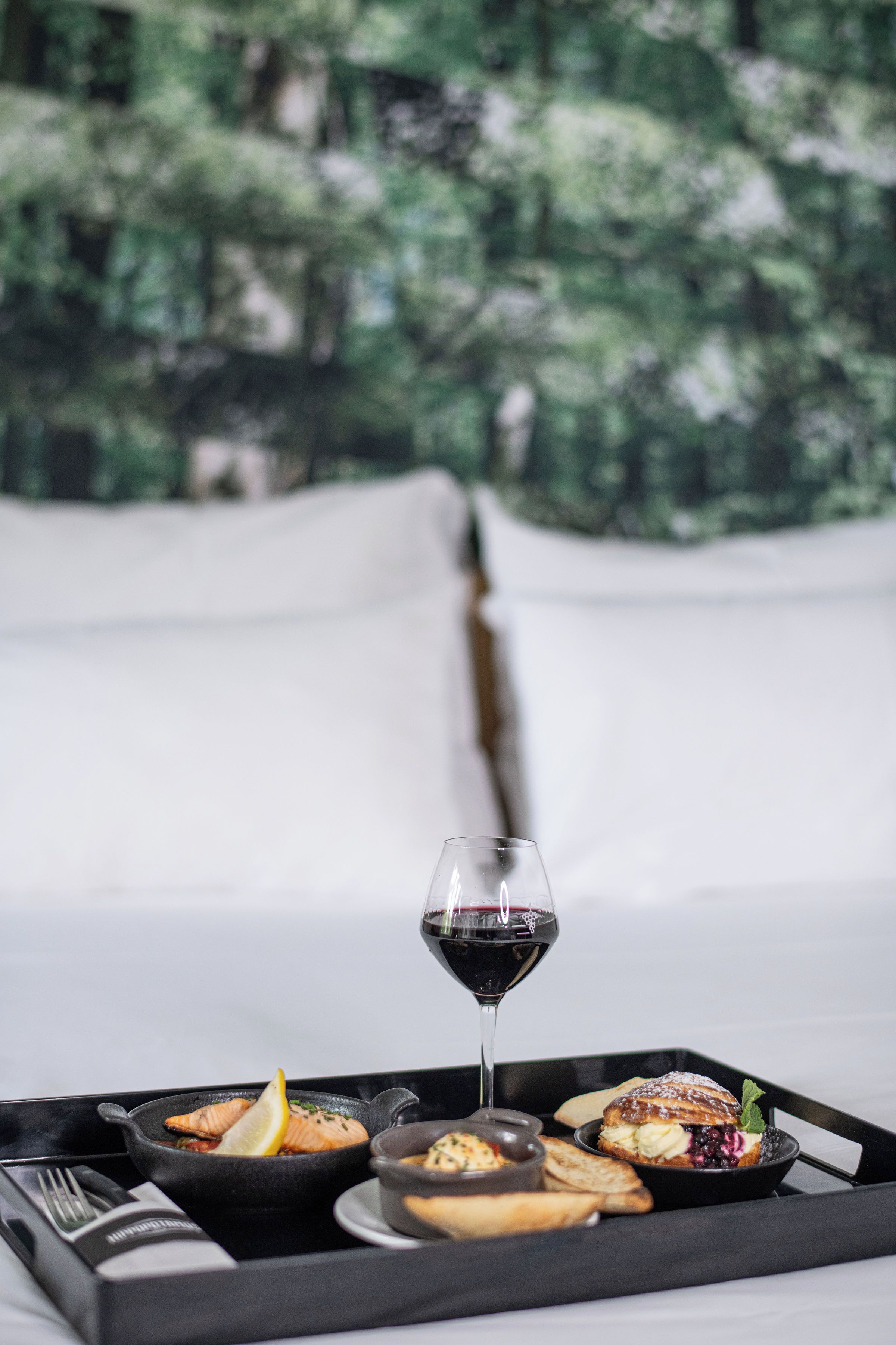 A tray with food and a glass of red wine on a bed.