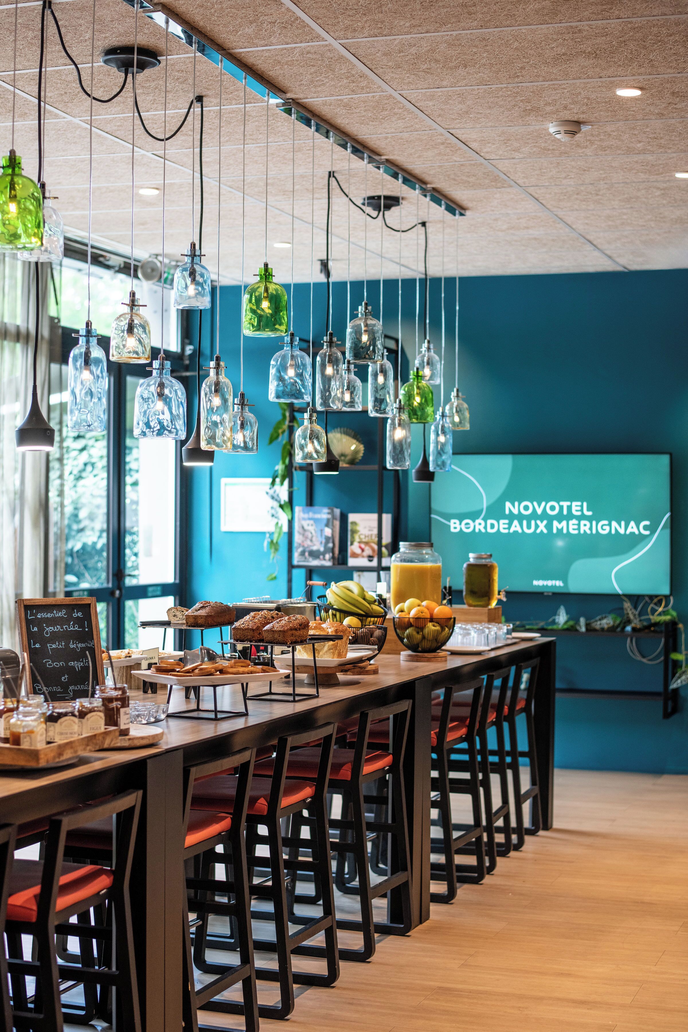 A restaurant with a long counter, hanging light fixtures, and a menu board.