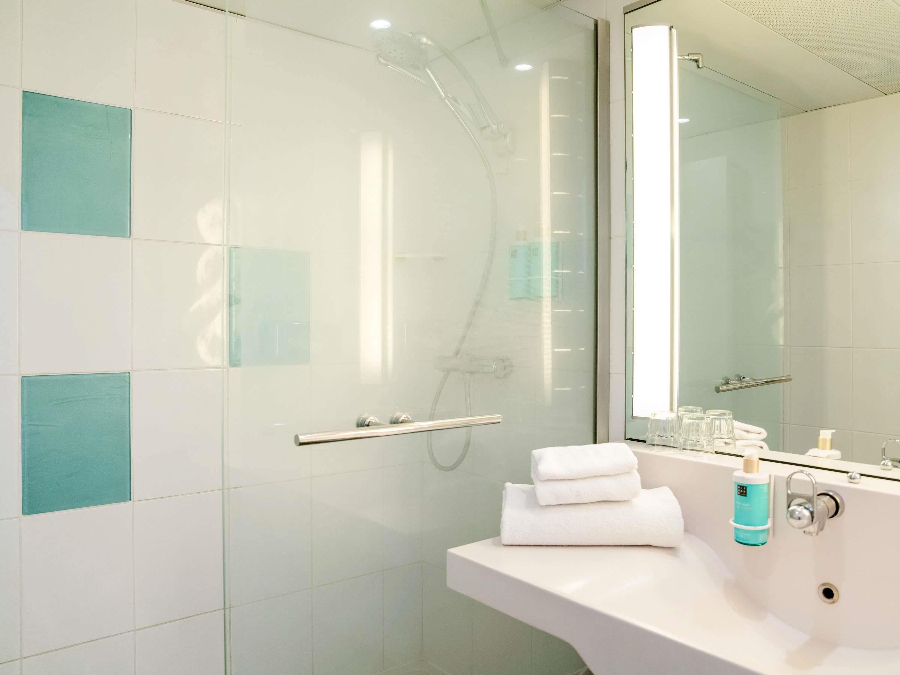 A modern bathroom with a glass shower enclosure, a white sink, and a mirror.
