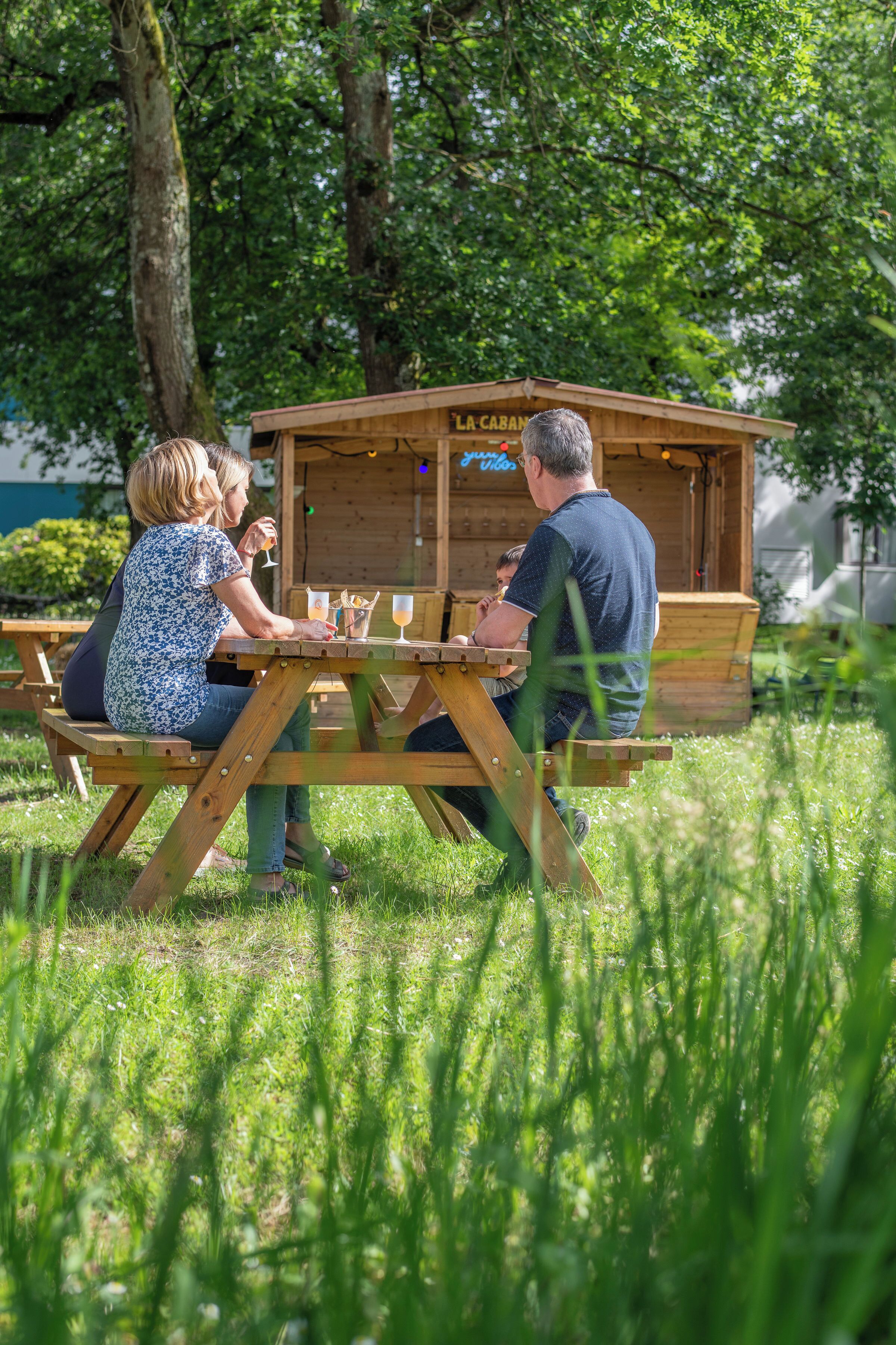 A wooden outdoor seating area with a table and benches, surrounded by lush greenery.